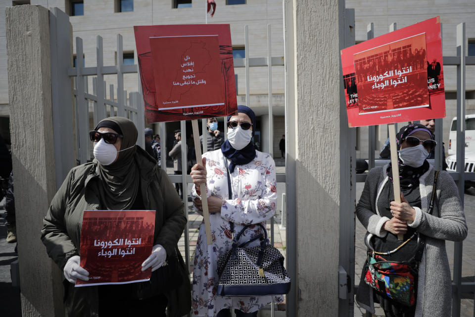 FILE - In this Feb. 26, 2020 file photo, anti-government protesters hold up banners in Arabic that read, "You are the coronavirus, you are the epidemic," and "Humiliation, bankruptcy, looting, starving and killing the rest of us," in front of the Lebanese Ministry of Health, in Beirut, Lebanon. As 2019 gave way to 2020 in a cloud of tear gas, and in some cases a hail of bullets - it seemed civil disobedience and government responses to protests would dominate the international landscape. Then came the Coronavirus. The protest camps in central Beirut are subdued. Masks worn to protect against tear gas are more often now worn to protect against the virus. The vast majority of people recover from the new virus. (AP Photo/Hassan Ammar, File)