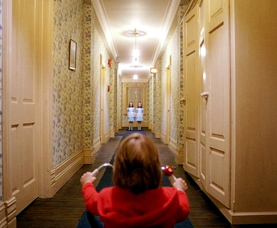 A little boy on a bike and twin girls at the end of the hall