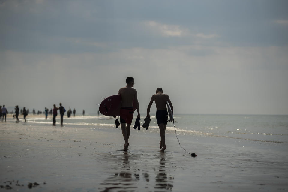 Two surfers walk along the sea shore during a partial lockdown to prevent the spread of coronavirus, COVID-19, in Oostende, northern Belgium, Thursday, May 21, 2020. Belgium is heading for a sun-drenched long weekend yet the government of the coastal province is imploring people to stay away even if they have a second residence in one of the many bathing resort towns. (AP Photo/Francisco Seco)