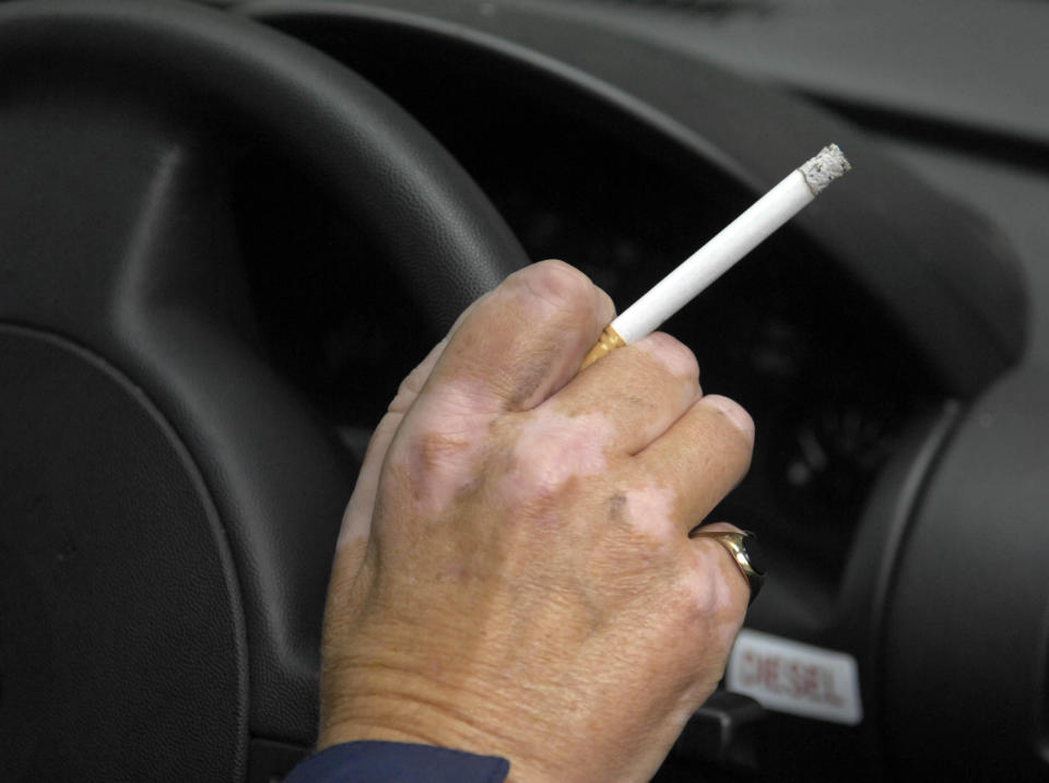 Man holding a cigarette while at the wheel of a car