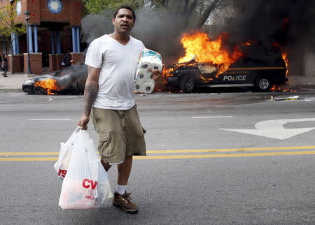 A man with goods looted from a store walks past burning vehicles during clashes in Baltimore, Maryland April 27, 2015. REUTERS/Shannon Stapleton