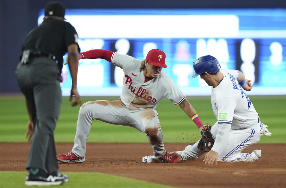 Philadelphia Phillies second baseman Bryson Stott, center, tags out Toronto Blue Jays' Daulton Varsho (25) trying to steal second base during seventh inning of a baseball game in Toronto on Tuesday, Aug. 15, 2023. (Nathan Denette/The Canadian Press via AP)