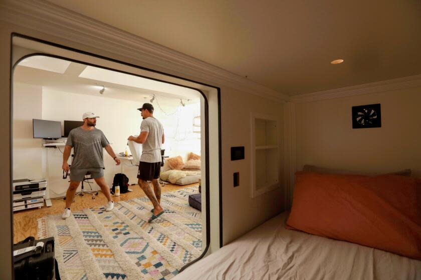 Two people standing in a room, seen through the doorway of a sleeping pod in a hotel.