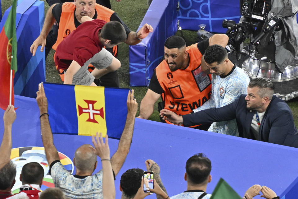 A boy crosses the barriers as Portugal's Cristiano Ronaldo, rear second right, leaves the pitch at the end of a Group F match between Georgia and Portugal at the Euro 2024 soccer tournament in Gelsenkirchen, Germany, Wednesday, June 26, 2024. (Bernd Thissen/dpa via AP)