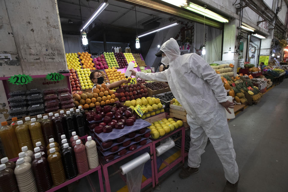 Un trabajador sanitario con equipo protector para reducir la propagación del nuevo coronavirus, provee alcohol a una vendedora para que desinfecte sus manos en el mercado conocido como Central de Abasto en la Ciudad de México, el jueves 18 de junio de 2020. (AP Foto/Marco Ugarte)
