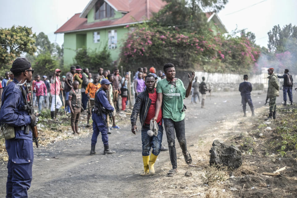 A wounded demonstrator walks past police officers during a protest against the United Nations peacekeeping force (MONUSCO) deployed in the Democratic Republic of the Congo in Sake, some 15 miles (24 kms) west of Goma, Wednesday July 27, 2022. Officials say more than 15 people have been killed and dozens injured during the demonstrations against the UN mission in the country, heading into their third day. (AP Photo/Moses Sawasawa)