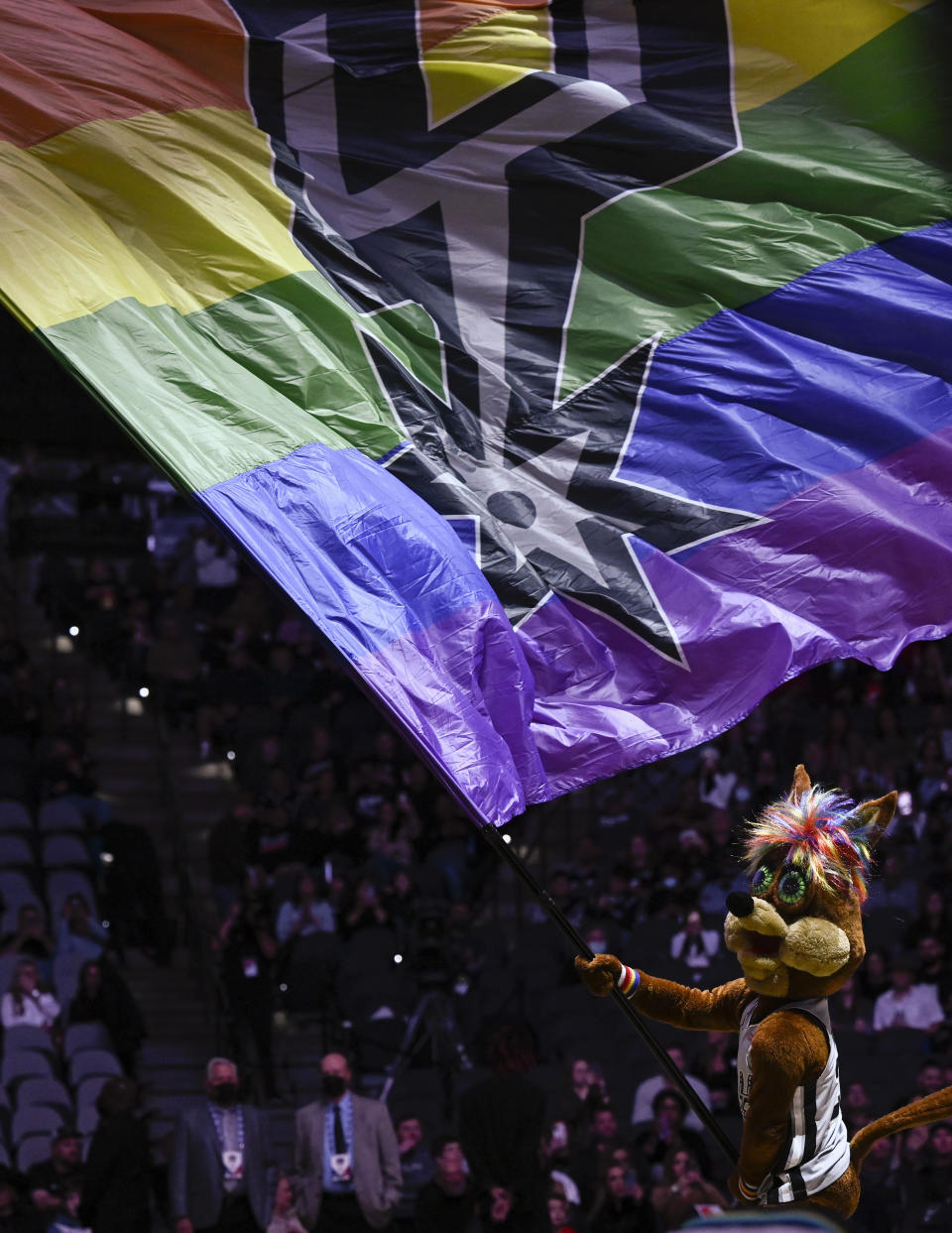 FILE - The San Antonio Spurs coyote mascot waves a giant rainbow flag in celebration of Spurs pride night before the start of an NBA basketball game against the Denver Nuggets, Saturday, Dec. 11, 2021, in San Antonio. The Texas Rangers have frustrated LGBTQ+ advocates for years as the only Major League Baseball team without a Pride Night. The June celebration of LGBTQ+ culture and rights known as Pride Month will come and go again without the Rangers participating. (AP Photo/Darren Abate, File)