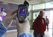 A Health Ministry staffer monitors the body temperature of travelers deplaning from international flights at the Mariscal Sucre Airport, in Quito, Ecuador, Saturday, Feb. 29, 2020. Officials in Ecuador on Saturday confirmed the first case of the new coronavirus in the South American nation. (AP Photo/Dolores Ochoa)