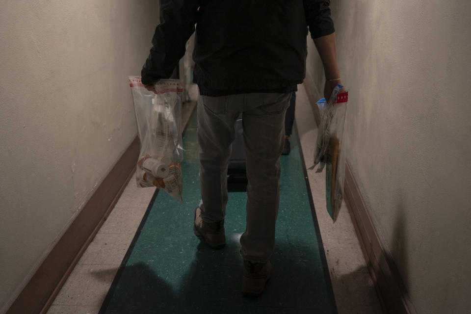 Dennis Cotek, an investigator with the Los Angeles County Public Administrator's office, carries plastic bags containing documents and personal belongings of a tenant in Los Angeles, Wednesday, Dec. 13, 2023. The tenant was found dead in his micro-apartment with no apparent next of kin. (AP Photo/Jae C. Hong)