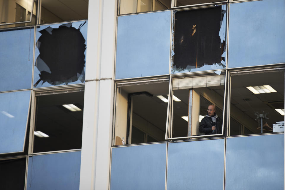 A journalist looks out a broken window after a powerful bomb exploded outside private Greek television station Skai, in Faliro, Athens, on Monday, Dec, 17, 2018. Police said the blast occurred outside the broadcasters' headquarters near Athens after telephoned warnings prompted authorities to evacuate the building, causing extensive damage but no injuries. (AP Photo/Petros Giannakouris)