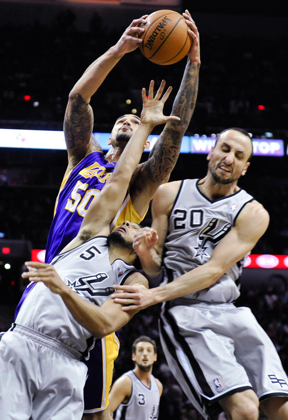 Los Angeles Lakers center Robert Sacre grabs a rebound over San Antonio Spurs guards Cory Joseph, left, and Manu Ginobili of Argentina during the second half of an NBA basketball game Friday, March 14, 2014, in San Antonio. (AP Photo/Bahram Mark Sobhani)