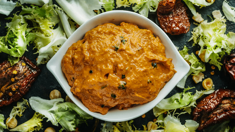 Bowl of romesco sauce sitting on a bed of salad
