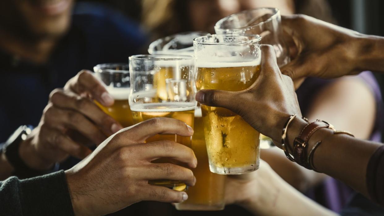 group of friends toasting beer glasses at table in bar