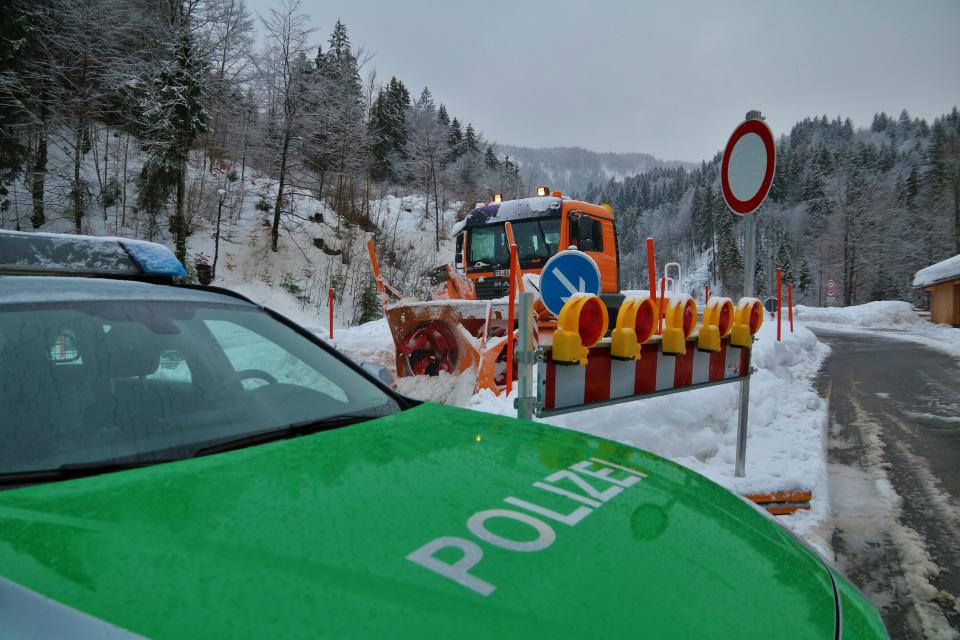 A police car blocks the street leading to Balderschwang as a snow plough passes by in Obermaiselstein, southern Germany, Monday, Jan. 14, 2019. (Benjamin Riss/dpa via AP)