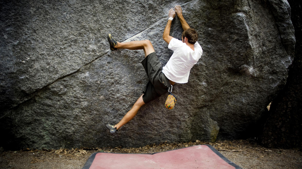  A climber performs a heel hook while bouldering over a red crash pad 