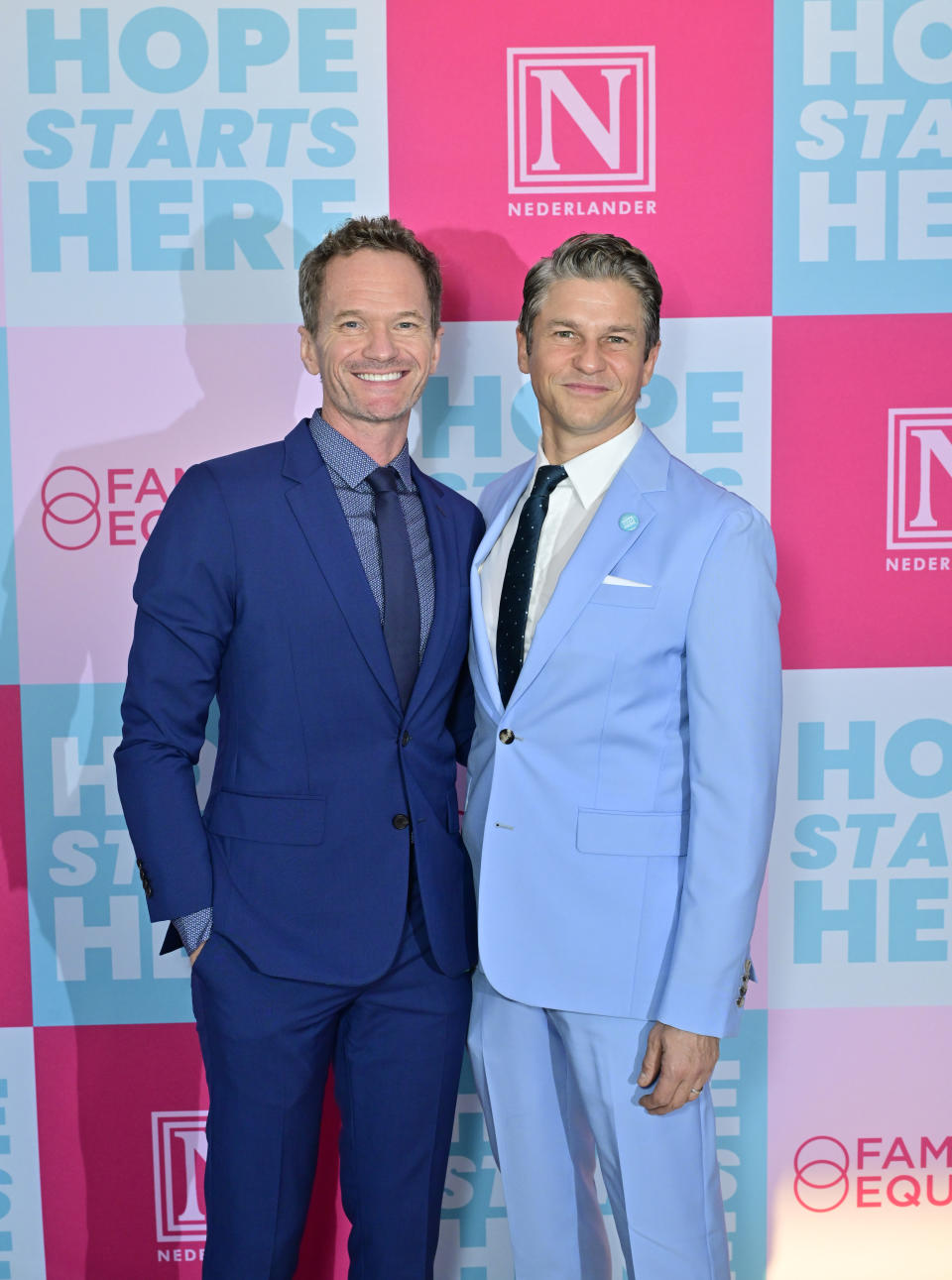 Neil Patrick Harris and David Burtka pose in blue suits at an event with a "Hope Starts Here" and "Nederlander" backdrop