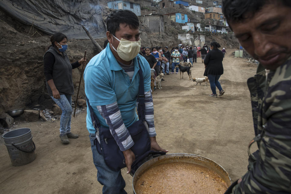 Los voluntarios llevan una olla de carapulcra, un guiso tradicional andino, a una mesa cercana mientras los residentes esperan en la fila para recibir un almuerzo gratis en una olla comunitaria en el barrio Nueva Esperanza de Lima, Perú, el sábado 6 de junio de 2020. (AP Foto/Rodrigo Abd)