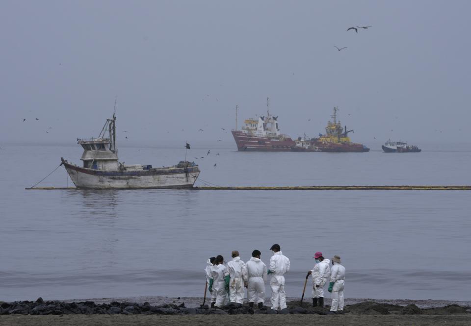 Workers, dressed in protective suits, continue to clean the oil contaminated Conchitas Beach, in Ancon, Peru, Thursday, Jan. 20, 2022. The oil spill on the Peruvian coast was caused by the waves from an eruption of an undersea volcano in the South Pacific nation of Tonga. (AP Photo/Martin Mejia)