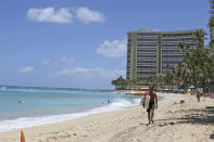 FILE - In this June 5, 2020, file photo, a surfer walks on a sparsely populated Waikiki Beach in Honolulu. Hawaii's governor says that starting Oct. 15, travelers arriving from out of state may bypass a 14-day quarantine requirement if they test negative for COVID-19. (AP Photo/Audrey McAvoy)