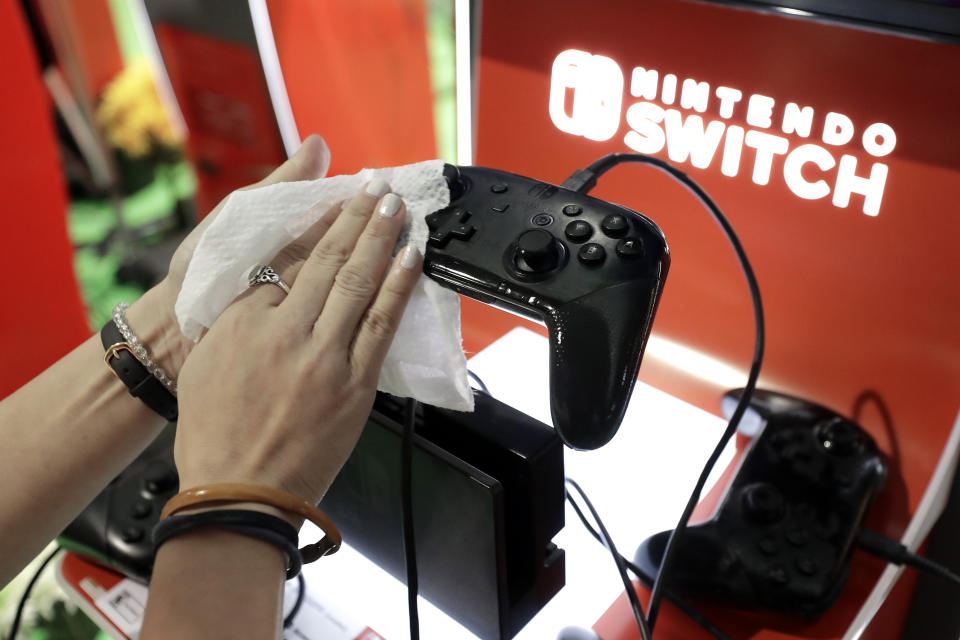 FILE - In this Feb. 27, 2020, file photo, game demonstrator Alex Chang uses a disinfectant wipe to clean a game console at the Nintendo Switch exhibit at the Pax East conference in Boston. Launched in 2017, the Switch became a fast seller. In March 2020, it became hard to find a Switch as people searched for ways to be entertained inside their homes. (AP Photo/Steven Senne, File)