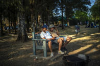 Two men watch a documentary on their cell phone as they join others celebrating South Africa's Heritage Day by cooking a barbecue at Zoo Lake park in Johannesburg Thursday Sept. 24, 2020. As the number of worldwide Covid-19 death is nearing the million mark, coronavirus related case numbers and deaths in South Africa hit the lowest in months. (AP Photo/Jerome Delay)