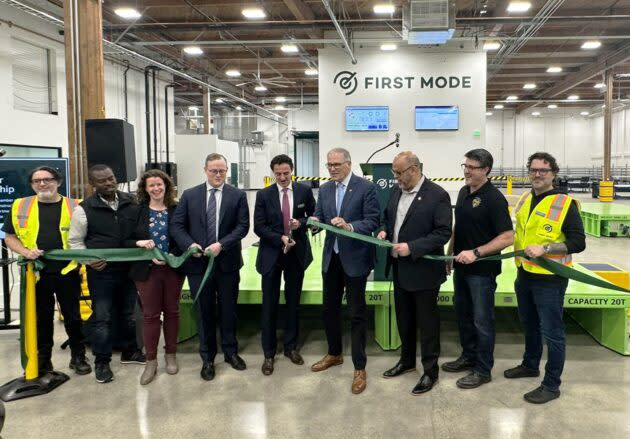 First Mode CEO Julian Soles wields a giant scissors at a factory ribbon-cutting ceremony with Washington Gov. Jay Inslee to the right and Albert Gore, executive director of the Zero Emission Transportation Association, to the left. (GeekWire Photo / Alan Boyle)