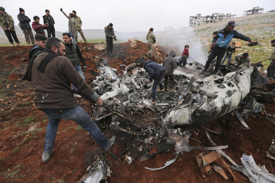 Syrians gather around a wreckage of a government military helicopter that was shot down in the countryside west of the city of Aleppo, Friday, Feb. 14, 2020. (AP Photo/Ghaith Alsayed)