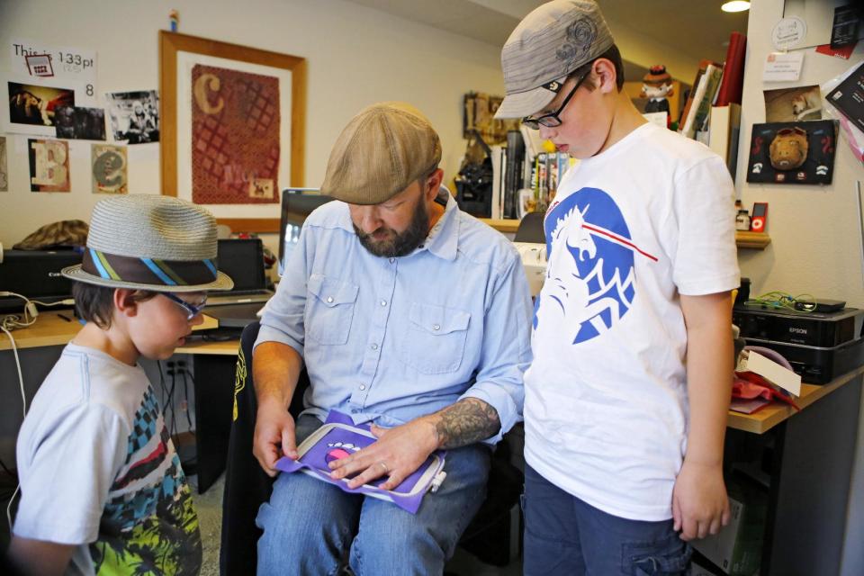 This photo taken on May 23, 2013 shows Ray Tollison inserting material into a frame for sewing, as sons Sam, left, and Ben look on at their home in Fort Collins, Colo. The Tollisons launched Monster to Love, a company that makes plush monster toys. (AP Photo/Ed Andrieski)