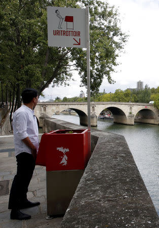 A journalist poses as he stands in front of a bright red, eco-friendly urinal on the Ile Saint-Louis along the Seine River in Paris, France, August 13, 2018. REUTERS/Philippe Wojazer