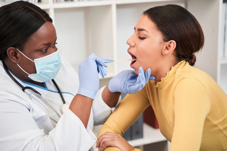 Close-up of brunette girl opening mouth while a doctor examines her sore throat. AdobeStock