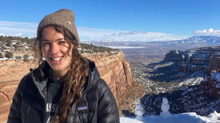 Woman stands smiling on red-canyon rim on sunny winter day.