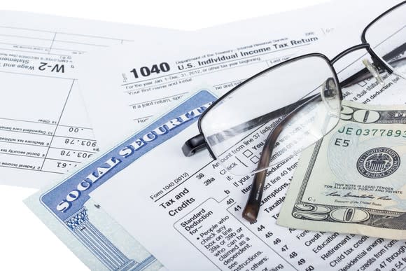 A Social Security card next to IRS tax forms, a pair of glasses, and a twenty dollar bill.