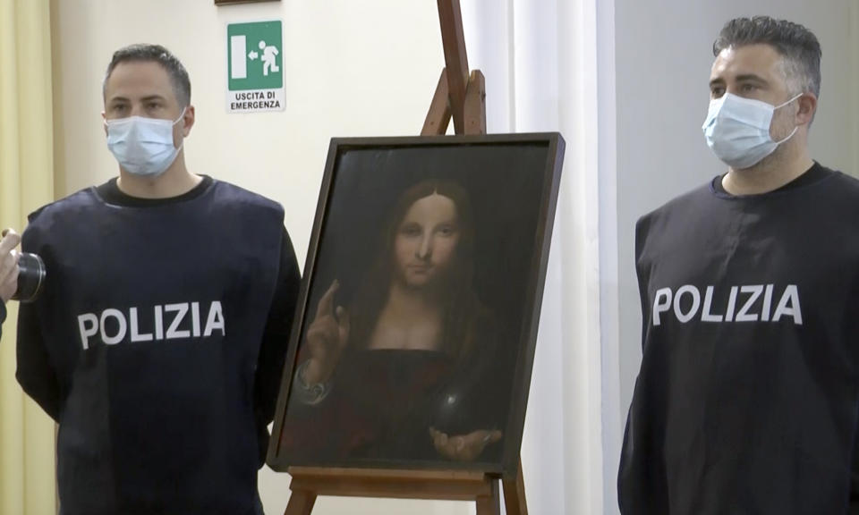 In this image taken from a video, two police officers pose by a copy of the “Salvator Mundi” (Savior of the World), by Leonardo da Vinci, in Naples, Italy, Wednesday, Jan. 20, 2021. Italian police have recovered a copy of Leonardo da Vinci’s 16th century “Salvator Mundi” painting of Jesus Christ that was stolen from a Naples church without the priests even realizing it was gone. The discovery was made over the weekend when Naples police working on a bigger operation found the painting hidden in an apartment. Police chief Alfredo Fabbrocini said the owner offered a “less than credible” explanation that he had “casually” bought it at a small market. (AP Photo/Sicomunicazione)