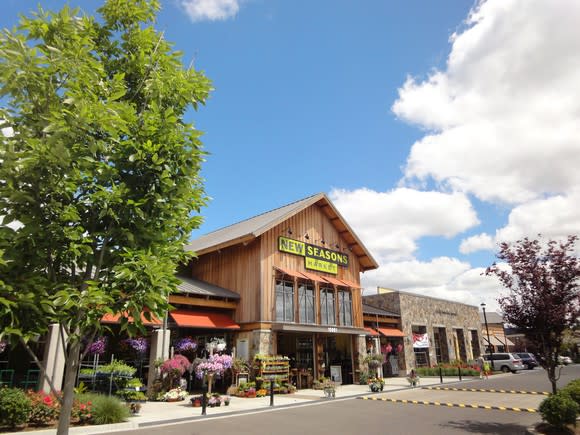 A grocery store named New Seasons Market with flowers and trees in front and under blue skies