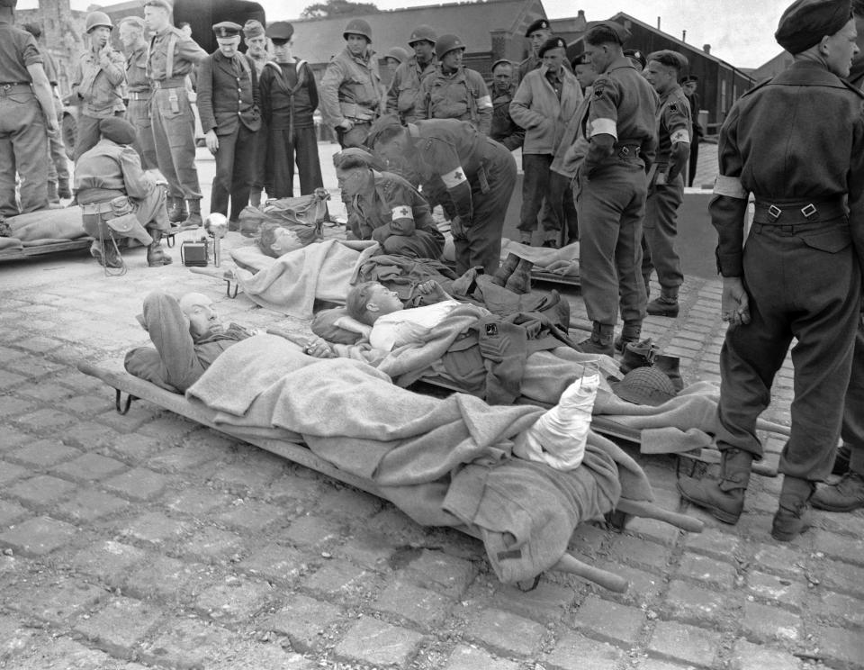 Some of the first British soldiers wounded in the French invasion coast fighting lie on stretchers somewhere in England, brought back the very day the assault started, June 6, 1944. Allied service men look with commiseration on their stricken comrades.