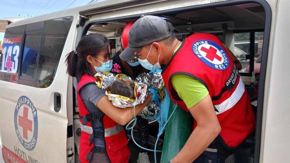 Philippine Red Cross workers carrying a child wrapped in an emergency blanket out of a van
