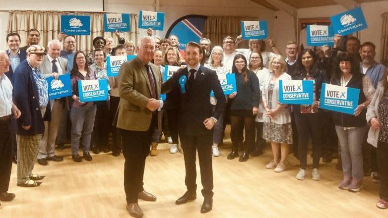 Sir Mike Penning and Jaymey McIvor shaking hands and standing in front of a group of people