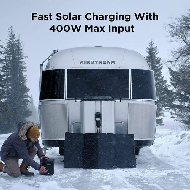 A person connects a portable solar panel to an Airstream trailer in a snowy setting. Text: Fast Solar Charging With 400W Max Input