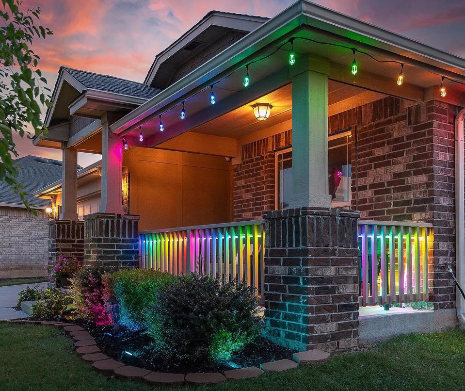 House's front porch and bushes lit in rainbow colors by LED string lights