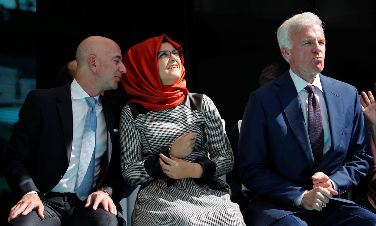 Jeff Bezos, leans over to whisper something to his neighbor, Hatice Cengiz, whose head is covered by a scarf, and who is also seated next to Fred Ryan.