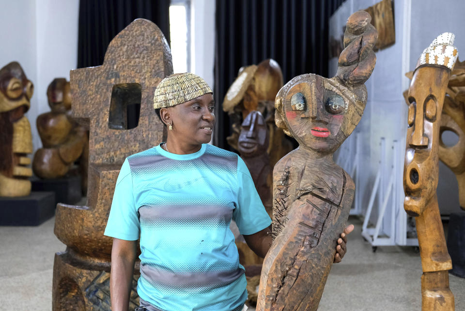 Lilian Nabulime stands next to a wooden sculpture piece at her workshop in Kyanja, a suburb in Kampala City, Wednesday Nov. 29 2023. Lilian Nabulime hasn't forgotten the time in the 1990s when the Ugandan capital had just one commercial art gallery, a small space that emerging artists struggled to get into. Now there are at least six in Kampala, including one whose curators recently exhibited the sculptor's contrarian work. (AP Photo/Hajarah Nalwadda.)