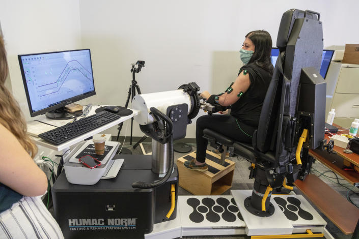 In this photo provided by UPMC and Pitt Health Sciences, research participant Heather Rendulic takes a test to measure arm strength in Pittsburgh on May 19, 2021. A stroke left Rendulic with little use of her left hand and arm, so she volunteered for a first-of-its-kind experiment that stimulates her spinal cord in spots that control upper limb motion. (Tim Betler/UPMC and Pitt Health Sciences via AP)