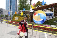 A man selling Chinese drums walk past a decoration promoting the upcoming Road and Belt Forum in Beijing on Friday, April 19, 2019. China is downplaying the political implications of its global development campaign known as the Belt and Road initiative, saying that it aims to boost multilateralism amid protectionist trends in the U.S. and elsewhere. (AP Photo/Ng Han Guan)