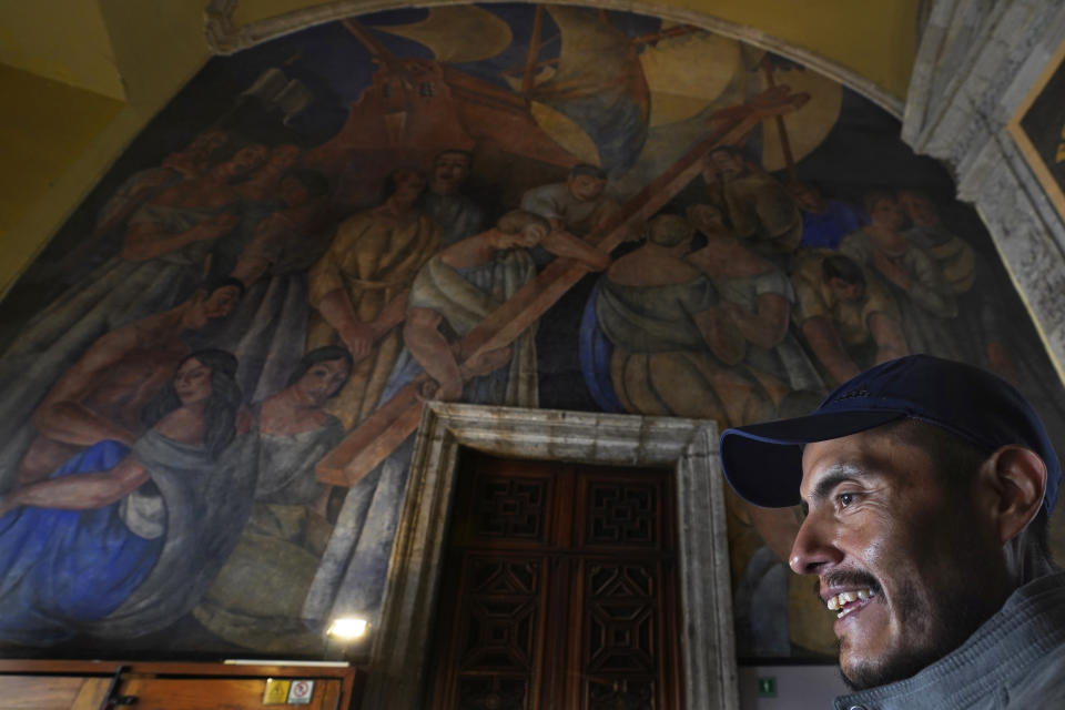 Historian Jonatan Chavez smiles backdropped by a mural by Ramon Alva de la Canal, titled, “The Landing of the Spaniards and the Cross Planted in New Lands”, in the former Jesuit college Antiguo Colegio de San Ildefonso in Mexico City, Wednesday, April 26, 2023. According to Chavez, murals like these will never lose relevance because they are a way to understand how history triggers a constant redefinition of spaces. “Our past is important because it speaks of our present,” he said. “These murals tell a lot about who we are and what we are made of.” (AP Photo/Marco Ugarte)