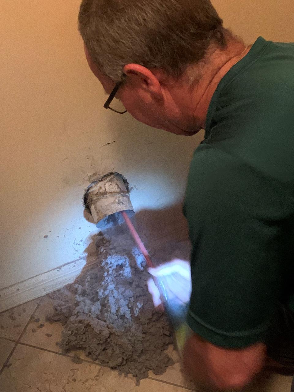 Ryan Arledge uses a drill and long, thin, flexible sticks with brushes attached to clean the inside of a dryer exhaust vent July 7, 2023.