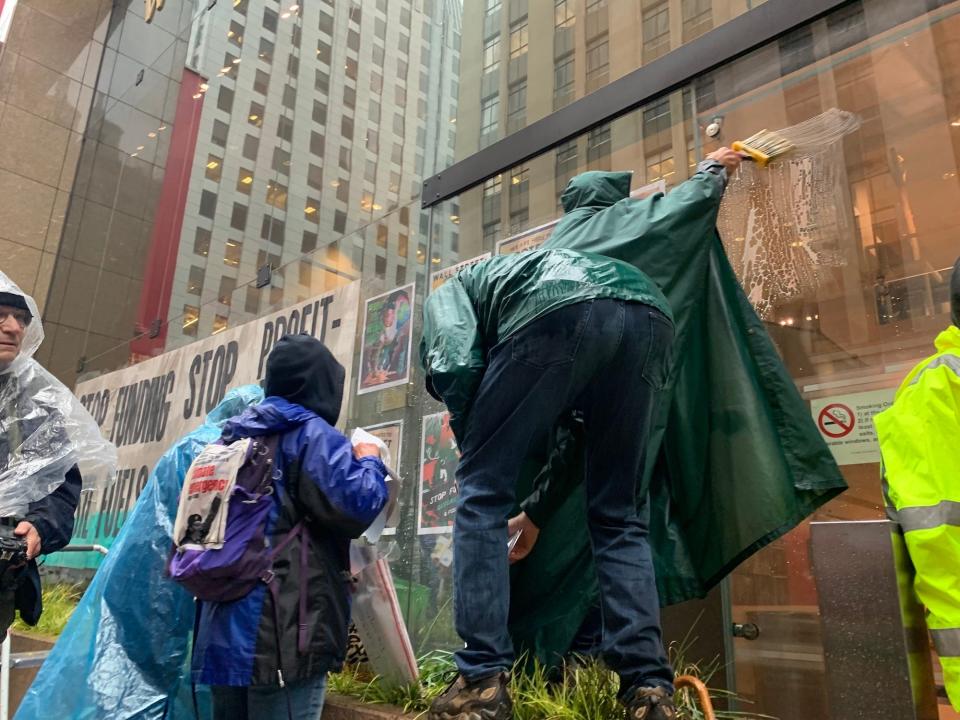 people in rain jackets ponchos paint glue onto glass business windows and hang protest signs