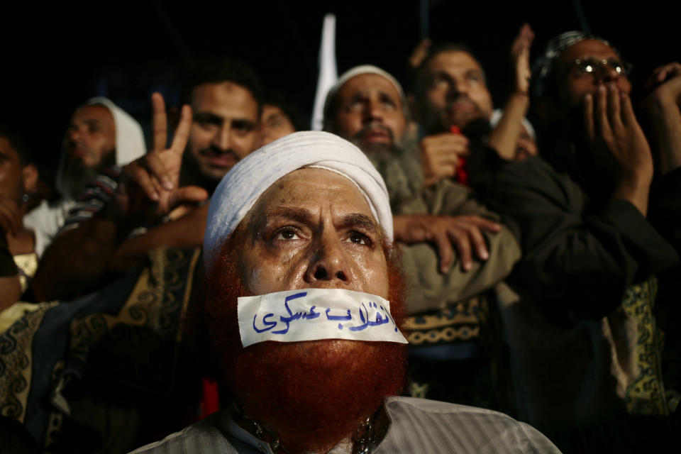 A supporter of Egypt's ousted President Mohammed Morsi covers his mouth with tape with Arabic writing that reads: "Military Coup," as others chant slogans against Egyptian Defense Minister Gen. Abdel-Fattah el-Sissi at Rabaah al-Adawiya mosque, where supporters of Egypt's ousted President Mohammed Morsi have installed a camp and hold daily rallies at Nasr City, in Cairo, Egypt, Thursday, Aug. 1, 2013. (AP Photo/Hassan Ammar)