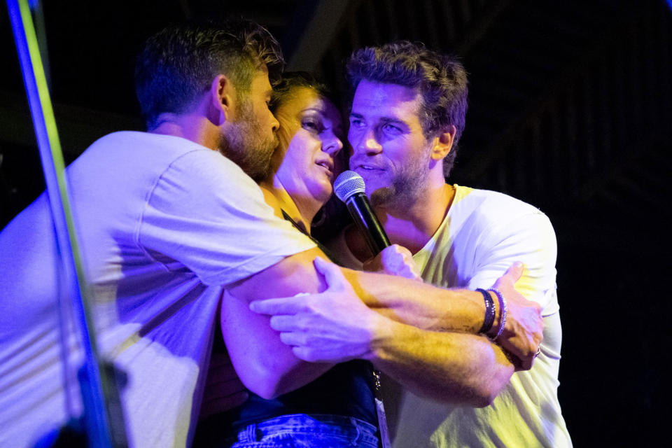 Celeste Barber hugs Chris and Liam Hemsworth on stage in Byron Bay