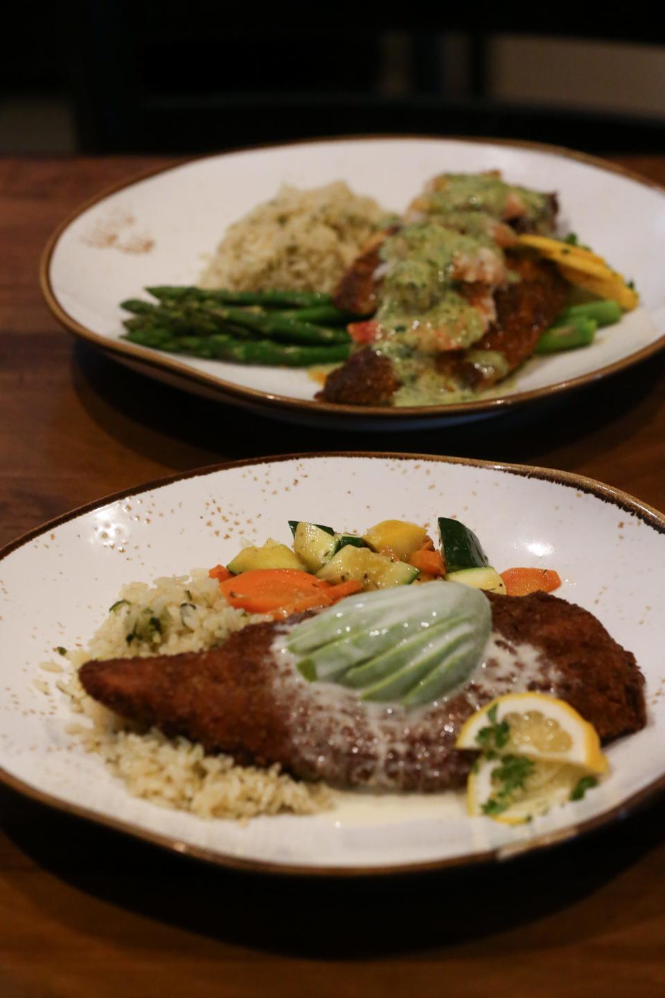 In front, the Pecan Snapper plate, and the Drum Parmesan plate, in the back, sit on a table at The Blue Clove Seafood Bar and Grill in The Market on Everhart Friday, May 3, 2024. Both dishes come with a rice pilaf and either a veggie medley or asparagus.
