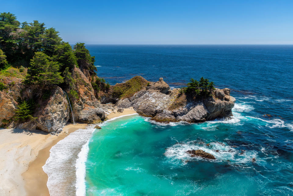 Coastal landscape with a waterfall emptying into the ocean, surrounded by forested cliffs